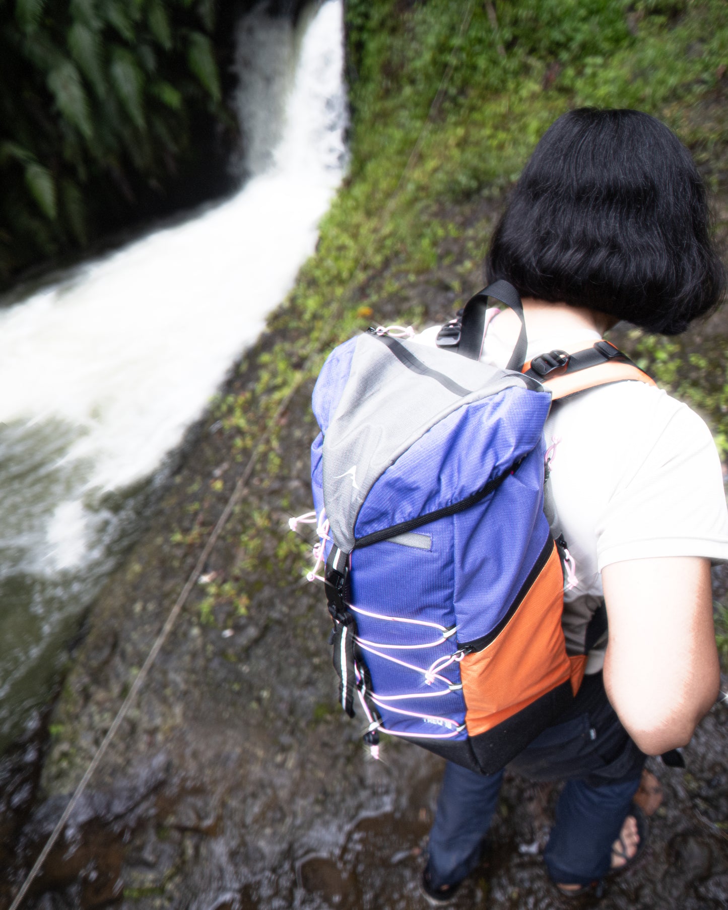A person exploring near a waterfall with the TREQ WILDFLARE Trail 22L Outdoor Backpack, illustrating its functionality in outdoor activities.