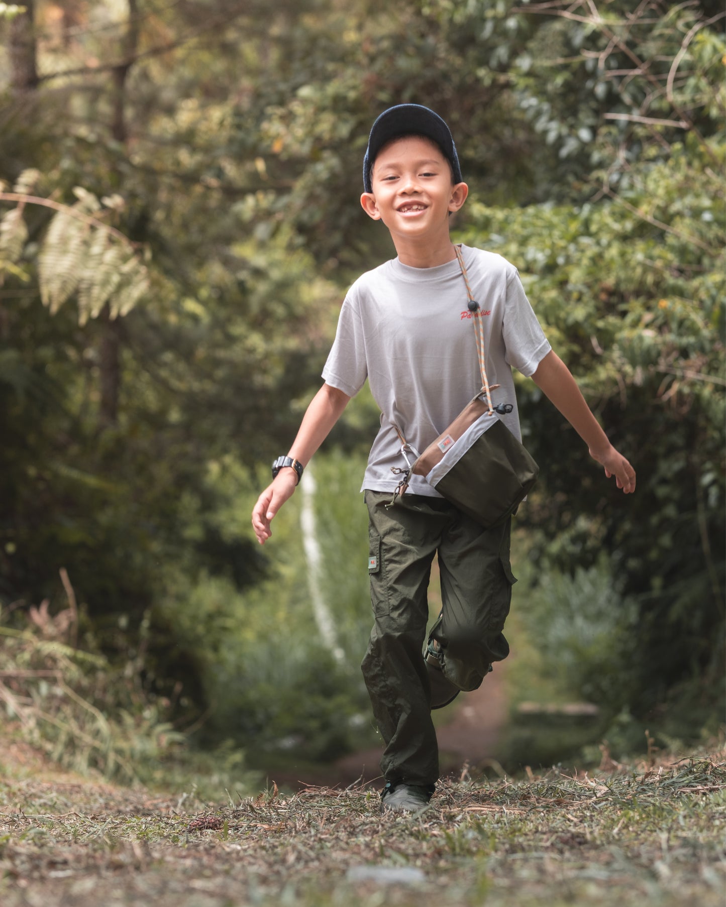 A young boy joyfully running down a forest path wearing the PIXIES Nutty Sprout bag. The lightweight, water-resistant bag complements his adventurous spirit as he explores the outdoors.