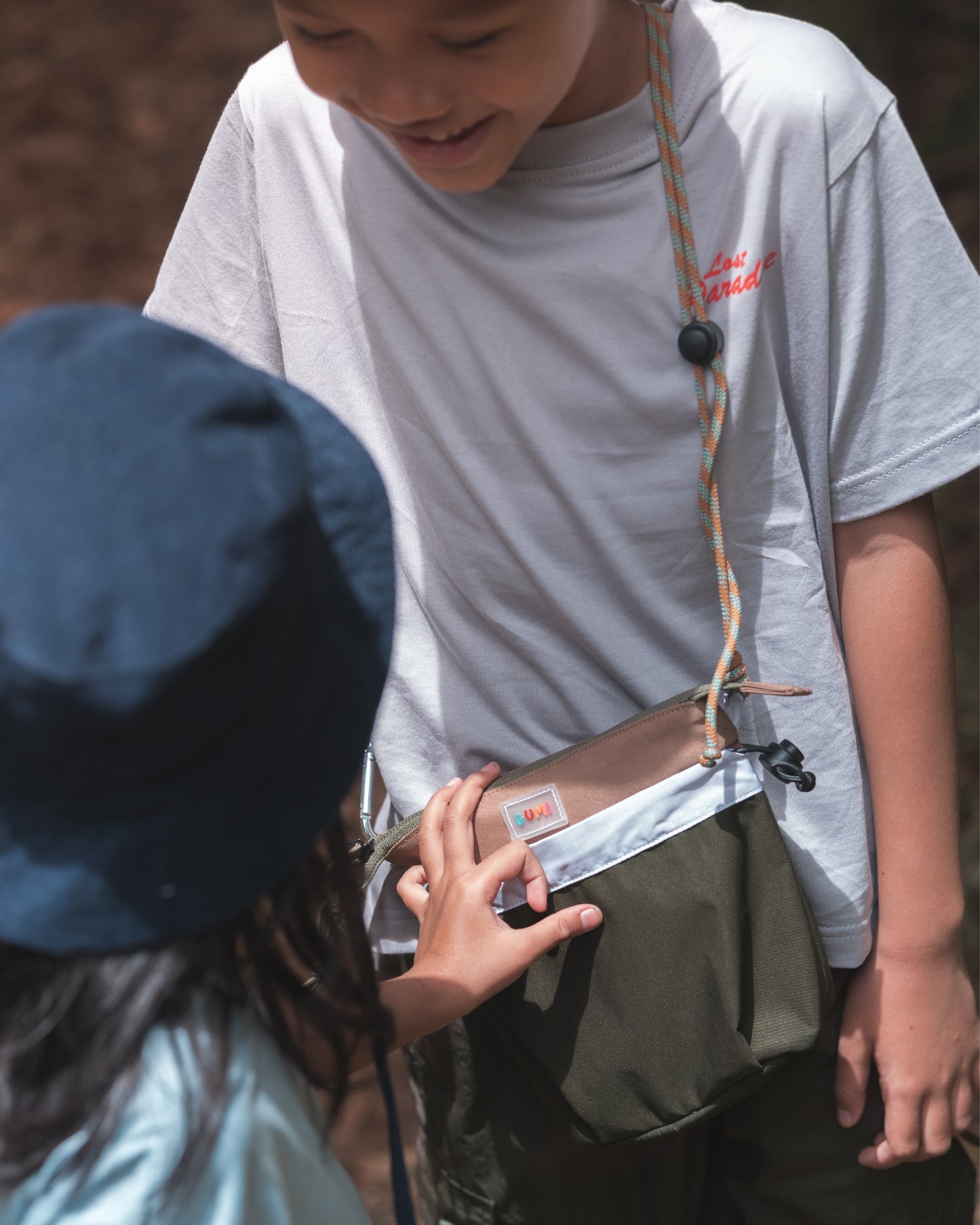Two children interacting in a playful moment, featuring the boy with the PIXIES Nutty Sprout bag. This fun accessory encourages kids to carry their belongings with comfort and confidence.