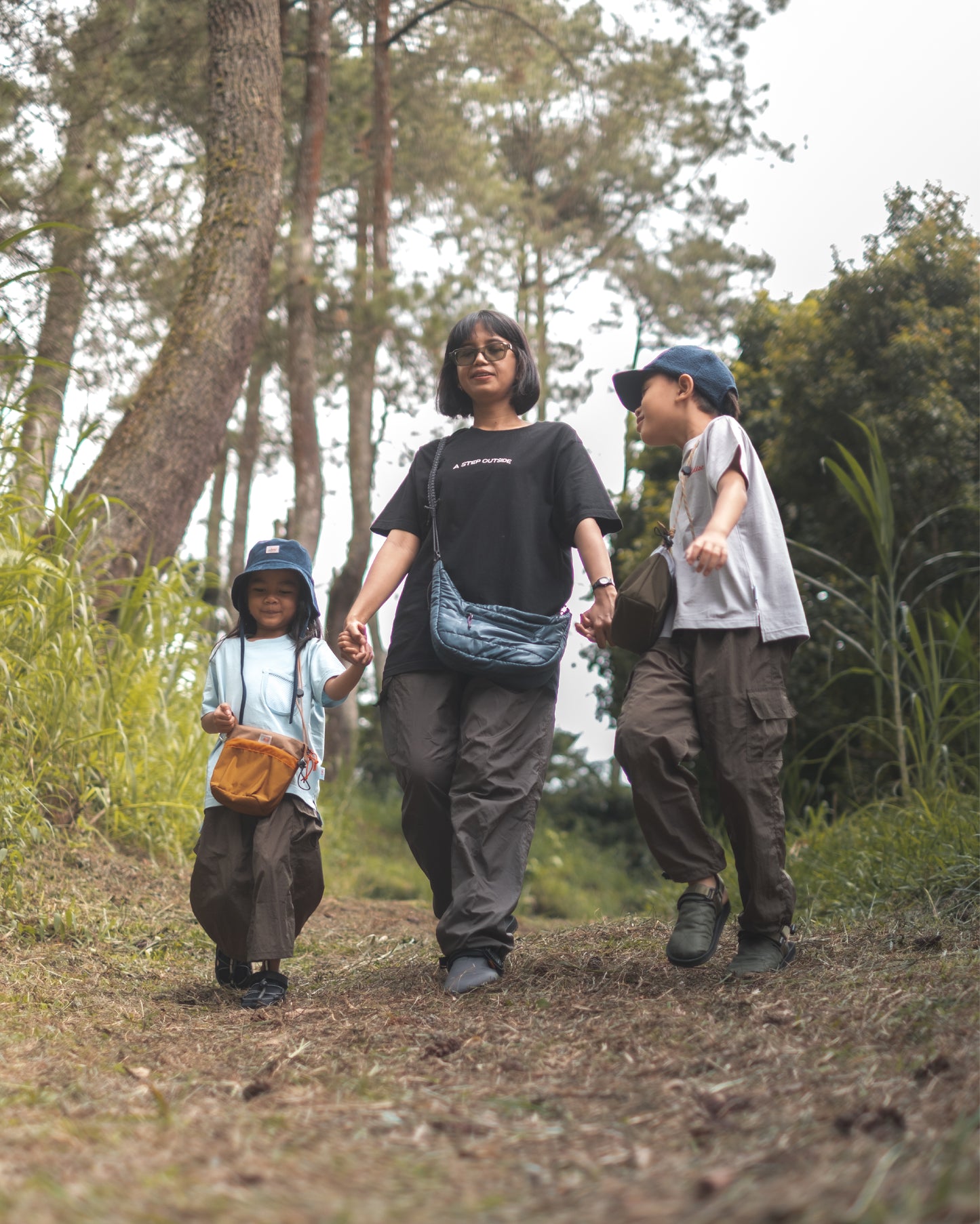 A family walking through a forest trail, with the kids proudly wearing the PIXIES Nutty Sprout bags for their outdoor fun.