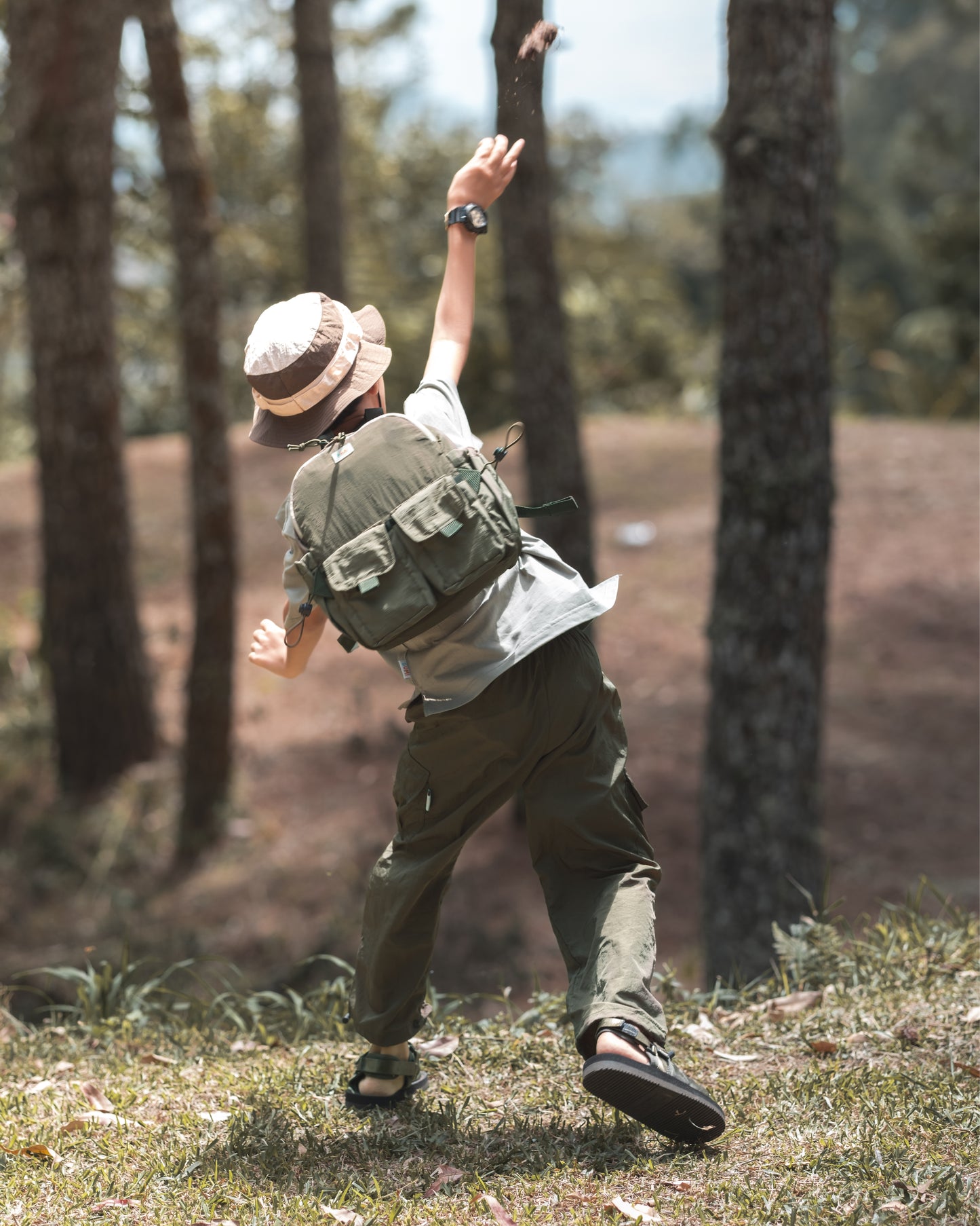 Child in green clothing turning to look back while wearing the VENEX Dewy Drip Mini Backpack for Kids, set against a natural backdrop, emphasizing the backpack's functionality.