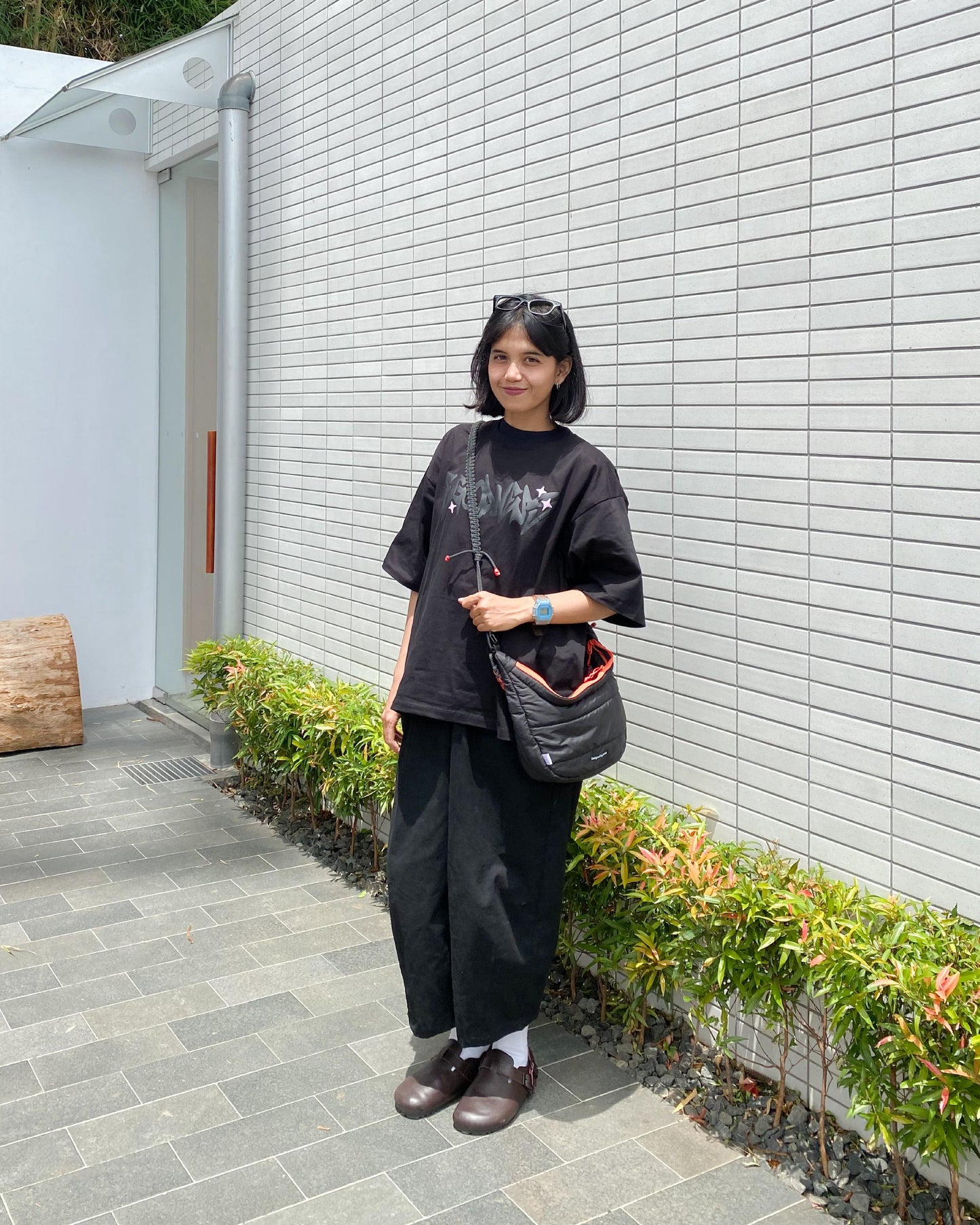 A young woman wearing the QUITAN Abyss Padded Crossbody Bag while standing outdoors, demonstrating its casual style.
