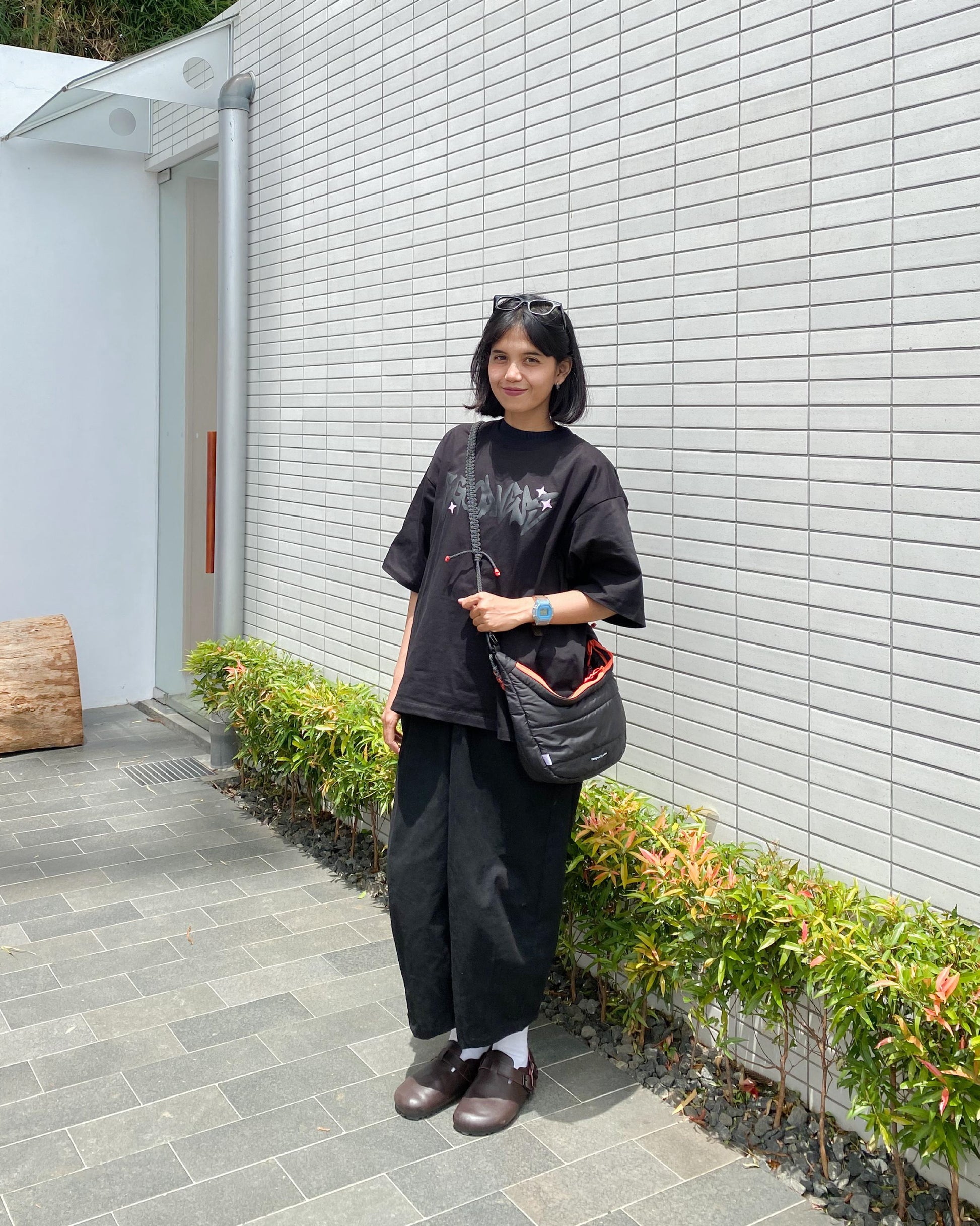 A young woman wearing the QUITAN Abyss Padded Crossbody Bag while standing outdoors, demonstrating its casual style.